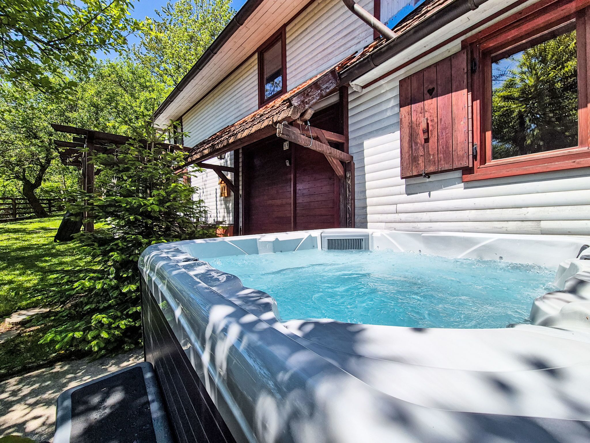 A hot tub in front of a wooden house with a red door and windows.