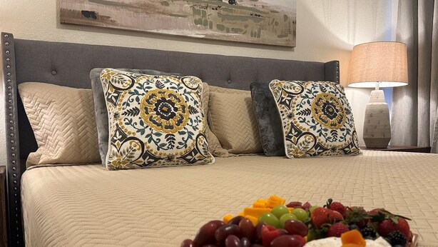 Ein Hotelzimmer mit einem Bett, Dekokissen, einer Obstplatte und einer Lampe.