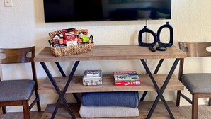 Ein Wohnzimmer mit einem an der Wand befestigten Flachbildfernseher, einem Couchtisch mit Snacks, einem Monopoly-Spiel und zwei Sesseln.