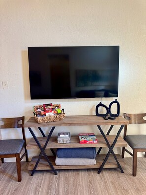 A living room with a flat-screen TV mounted on the wall, a wooden coffee table with snacks, a Monopoly board game, and two chairs. - Baylor House - Stylish Abilene Getaway (Abilene)