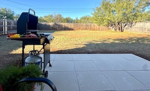 A backyard with a barbecue grill, a gas tank, and a table with vegetables. - Baylor House - Stylish Abilene Getaway (Abilene)