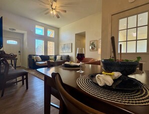 A dining area with a table set for two, a ceiling fan, and a view of the living room. - Baylor House - Stylish Abilene Getaway (Abilene)