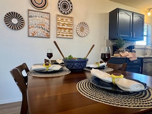 A dining table set with placemats, a bowl, and wine glasses, with a kitchen in the background. - Baylor House - Stylish Abilene Getaway (Abilene)