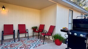 Eine Terrasse mit vier roten Stühlen, einem gemusterten Teppich und einem Grill.