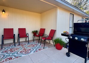A patio with four red chairs, a patterned rug, and a barbecue grill. - Baylor House - Stylish Abilene Getaway (Abilene)