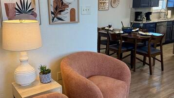 Un salon avec deux fauteuils, une table à manger avec des chaises, un coin cuisine et un lustre.