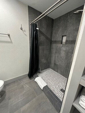 Een moderne badkamer met een douche, toilet en handdoekhouder.