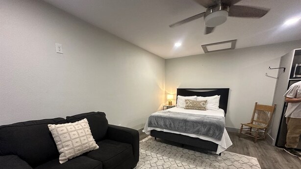 A bedroom with a bed, a black sofa, a wooden chair, and a ceiling fan. - Carriage House - Modern Downtown Studio (Abilene)