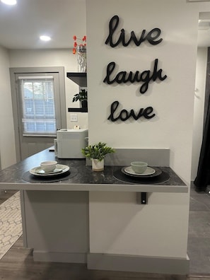Een keukenhoek met een aanrecht, een bordje aan de muur met de tekst 'live laugh love' en een plant in een pot.