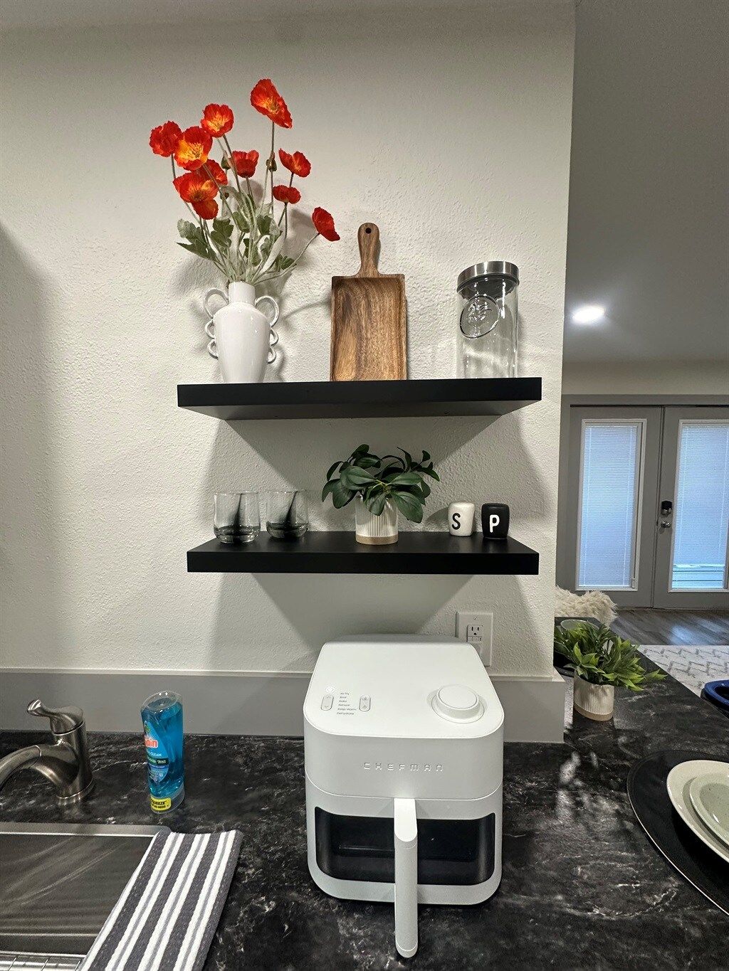 Une cuisine avec un plan de travail, un appareil électroménager blanc, un vase avec des fleurs rouges et une étagère contenant divers objets.