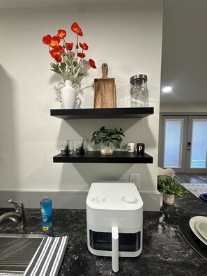 Una cocina con encimera, un electrodoméstico blanco, un florero con flores rojas y una estantería con diversos objetos.