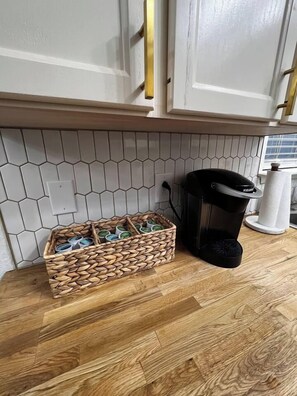 Una cocina con mostrador de madera, una cafetera y un cesto de cápsulas de café.