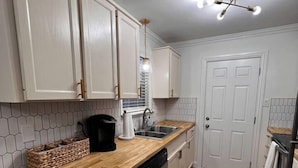 Una cocina compacta con armarios blancos, una encimera de madera, lavavajillas e iluminación en el techo.