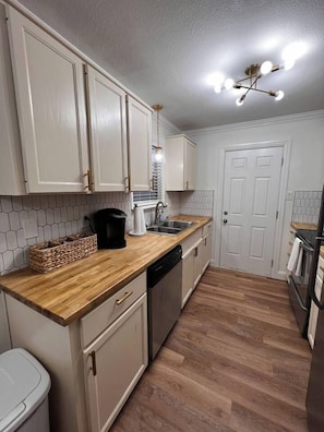 Una cocina compacta con armarios blancos, una encimera de madera, lavavajillas e iluminación en el techo.