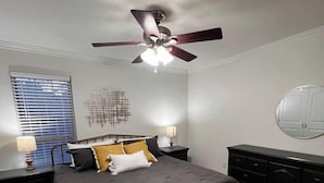 Un dormitorio con cama, ventilador de techo, cómoda y ventana con persianas.