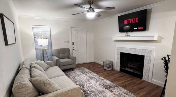Una sala de estar con sofá, sillón, chimenea, televisión y ventilador de techo.
