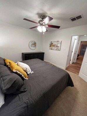 Un dormitorio con cama, ventilador de techo y puerta que da a otra habitación.