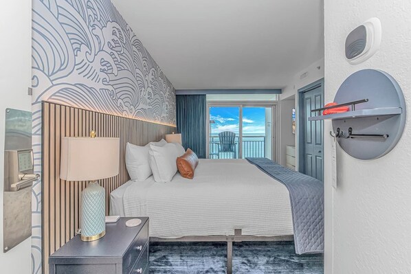 Ein Hotelzimmer mit einem Bett, einem Nachttisch, einer Lampe, Blick auf den Ozean und einem runden Wandregal.