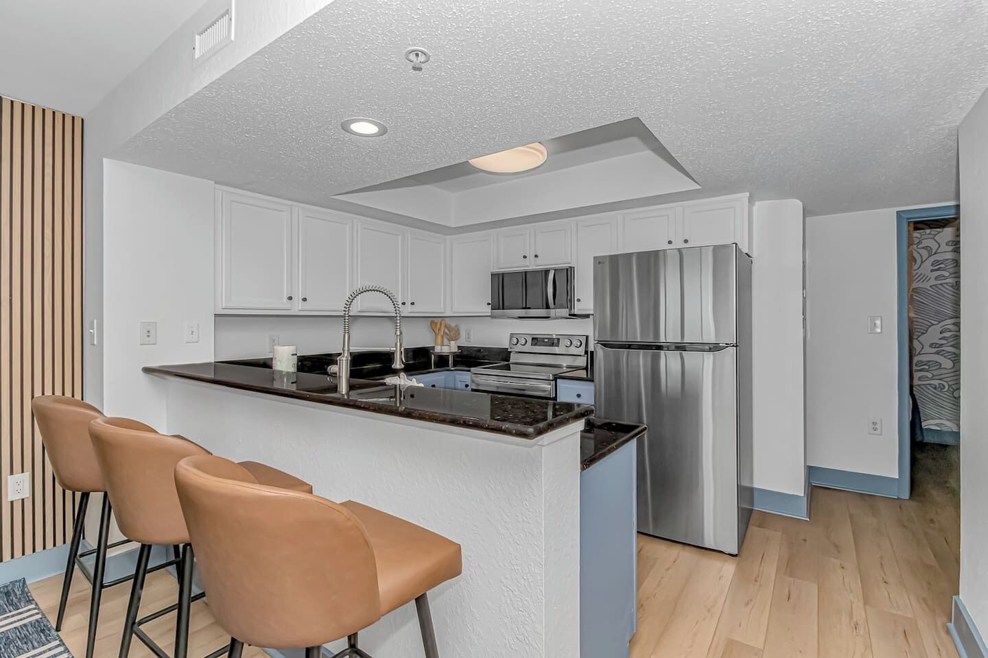 A modern kitchen with white cabinets, stainless steel appliances, and a bar area with two stools.