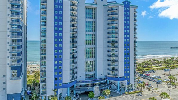 Un hotel de varios pisos con balcones, una zona de piscina y vistas a la playa.
