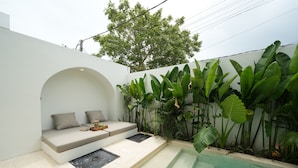 Un'area salotto esterna moderna con panchina integrata, un tavolino e una piscina.