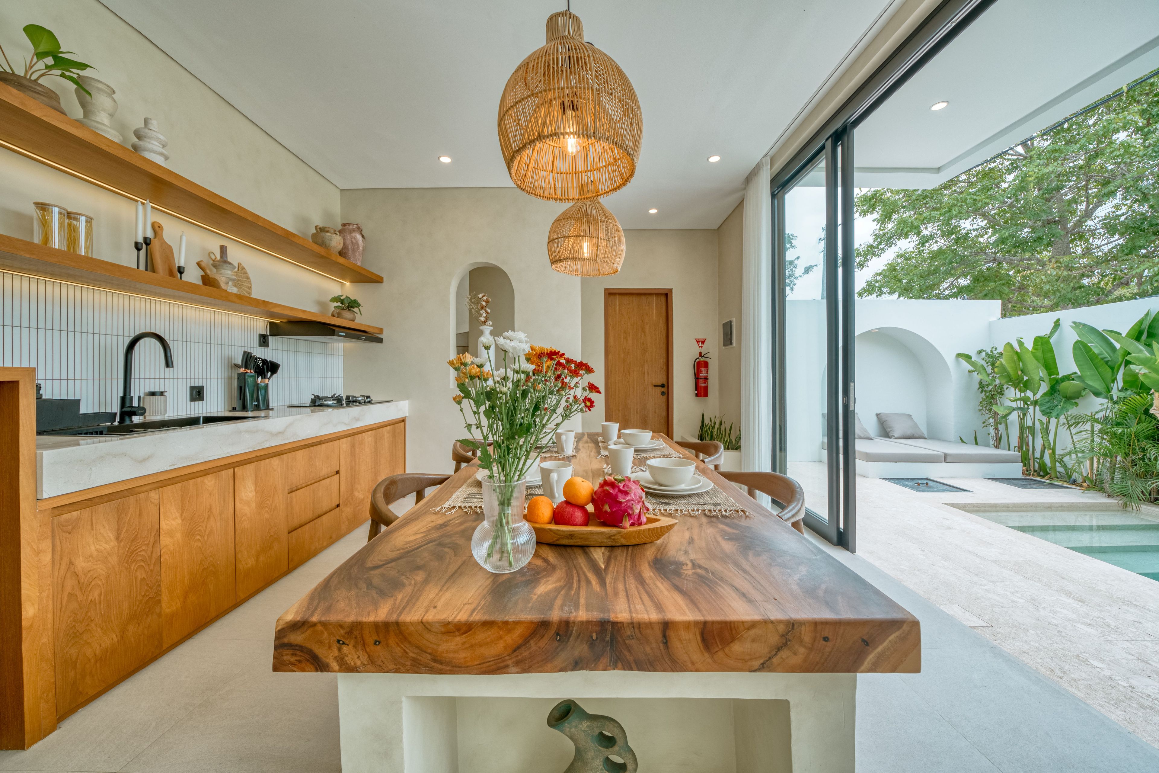 A modern kitchen with a wooden island, pendant lighting, and a dining area with a view of the outdoors.