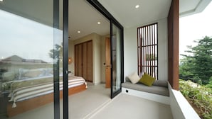 A modern bedroom with a glass door leading to a balcony, a bed with striped bedding, and a seating area with cushions. - Moraira 1BR Pool Villa Close to Bingin Beach (Pecatu)