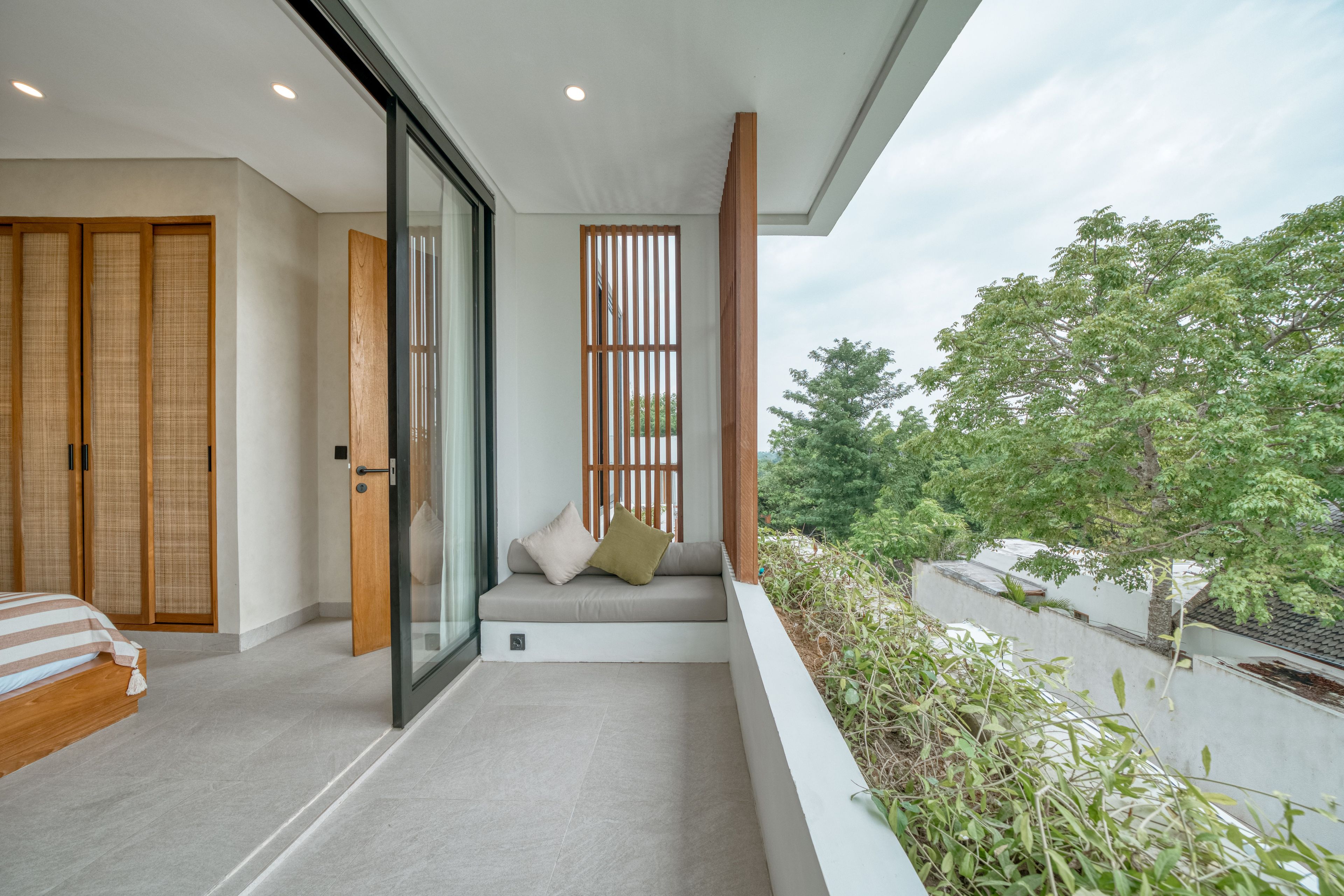 A modern balcony with a sofa, a sliding glass door, and a view of greenery.