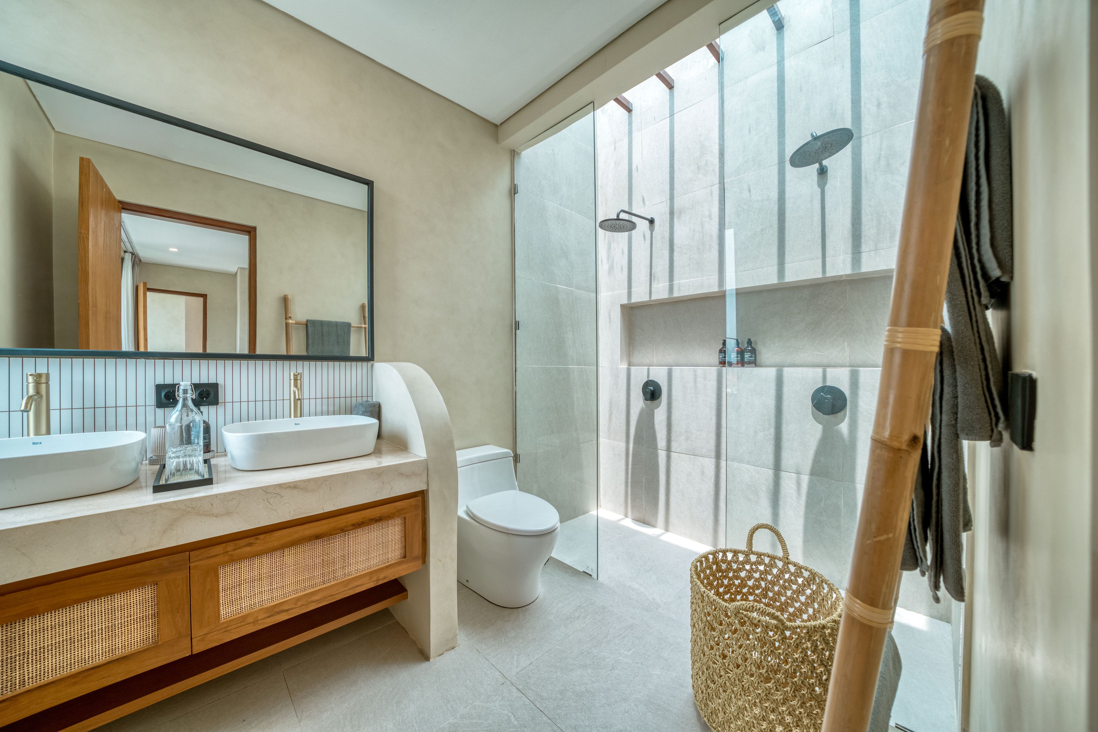 A modern bathroom with a large mirror, dual sinks, a toilet, and a glass-enclosed shower area.