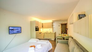 Hotellihuone, jossa on sänky, televisio, sohva, pieni keittiö ja ruokailutila.