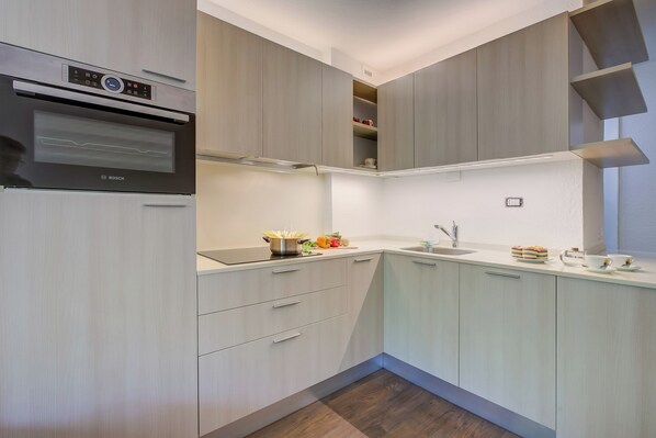 Una cucina moderna con elettrodomestici integrati, mobili chiari e un lavello d'angolo.