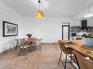 A dining area with a wooden table and chairs, a hanging light fixture, and a tiled floor. - Casa Verde | Historic House For 6 @ San German (San German)