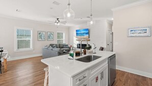 Een moderne keuken met een centraal eiland, een inbouwvaatwasser en een groot raam met zonwering.