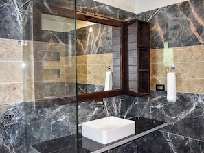 A bathroom with a glass enclosure, a white sink, and a mirror with a wooden frame. - Amaris Greens Resort (Ramnagar)