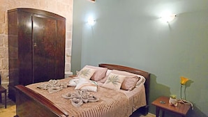 A bedroom with a wooden bed, a nightstand with a lamp, and a stone wall. - Traditional Maltese 2BR - Near Valletta (Floriana)