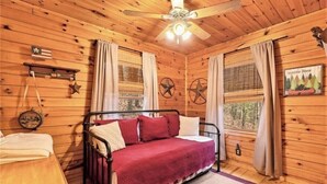 A cozy cabin room with a bed, wooden walls, a ceiling fan, and a window with curtains. - Mountain Heaven - Hot Tub - Pet Friendly - Long Range Mountain Views - Fire Pit (Blue Ridge)