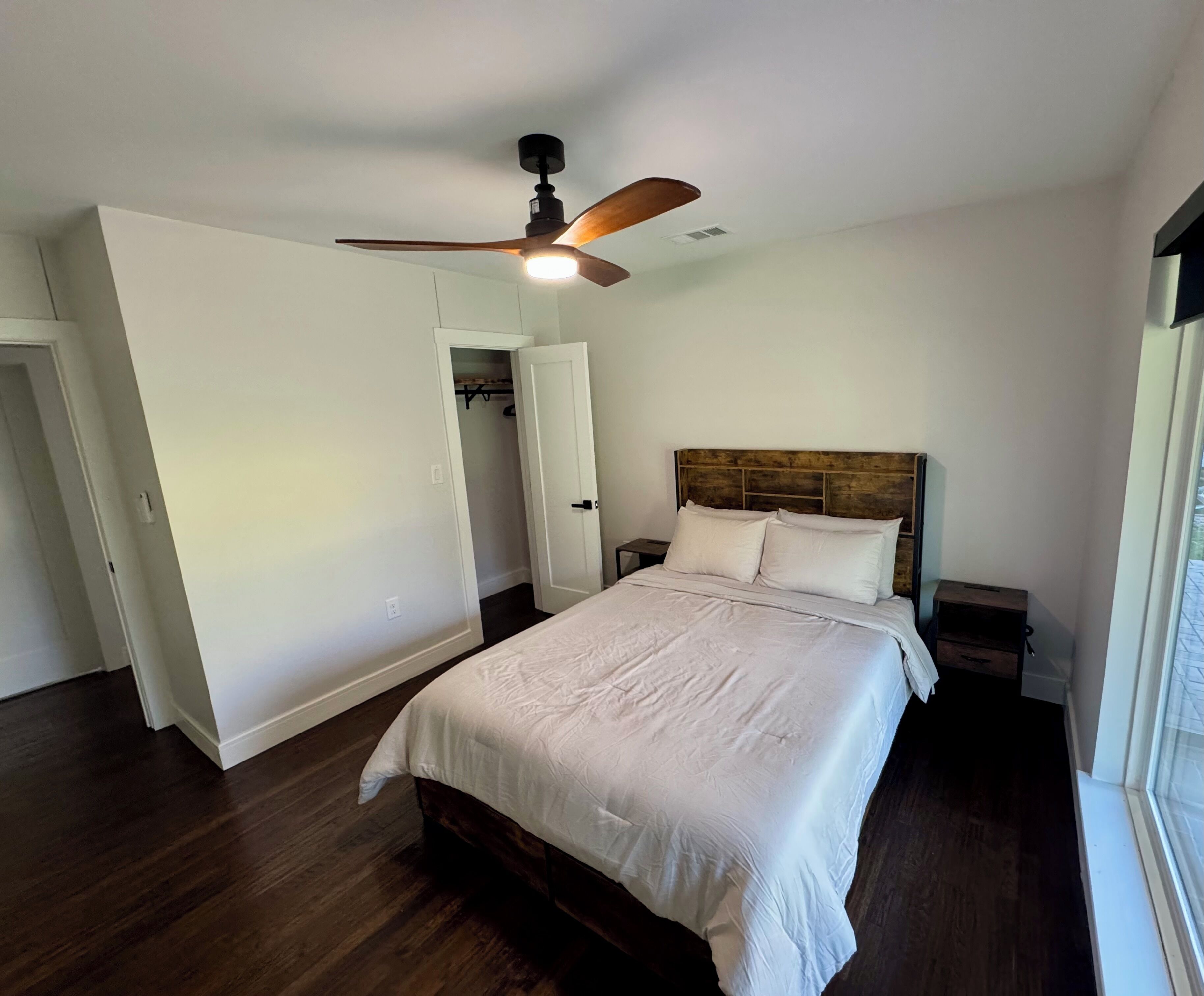 A bedroom with a wooden bed, a ceiling fan, a walk-in closet, and a window.