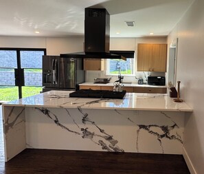 A modern kitchen with a marble island, stainless steel appliances, and wooden cabinets. - Warm & Modern Villa (Dallas)
