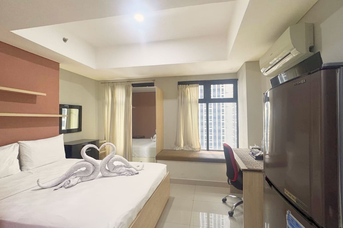 A hotel room with a bed, a desk with a computer, a refrigerator, and a window with curtains.