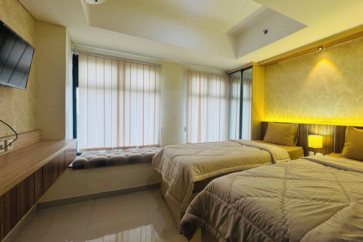 A hotel room with two beds, a seating area, a TV, and a window with blinds.