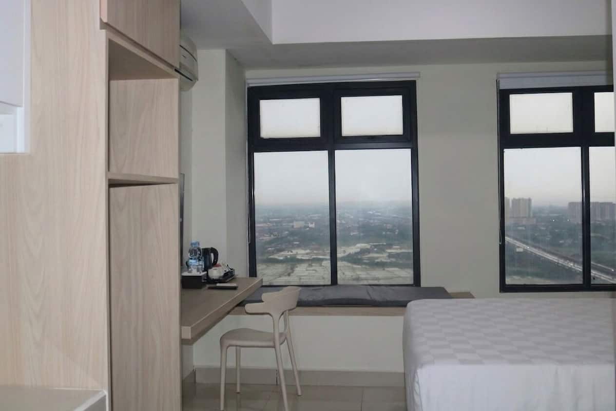 A hotel room with a bed, a desk with a chair, and large windows offering a city view.