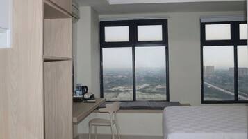 Une chambre d’hôtel avec un lit, un bureau et une chaise, ainsi que de grandes fenêtres donnant sur la ville.