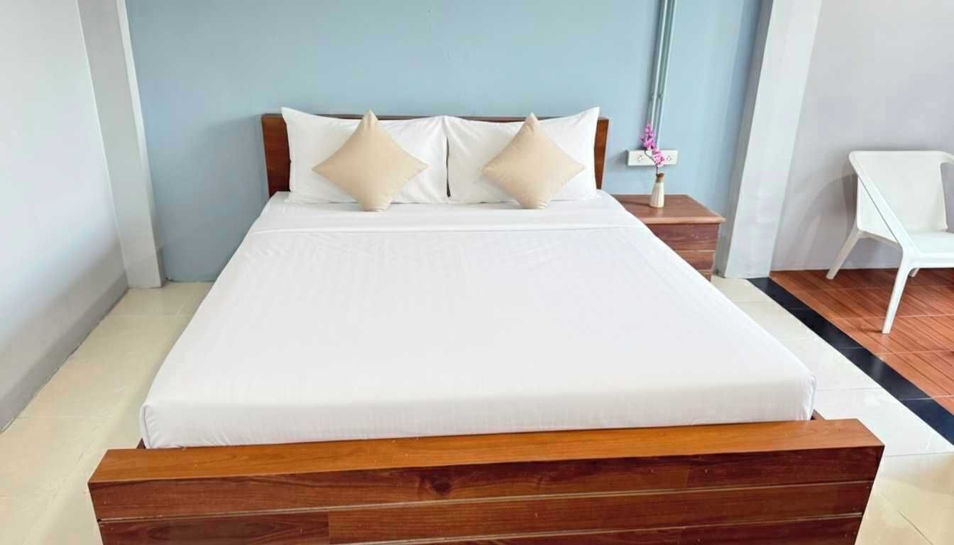 A neatly made bed with a wooden headboard, white bedding, and two beige pillows.