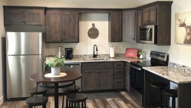 A modern kitchen with dark wooden cabinets, stainless steel appliances, a granite countertop, and a herringbone wood floor. - On The Banks Of The Salmon River 2bed/ 2bath/ Sleeps 6 (Salmon)