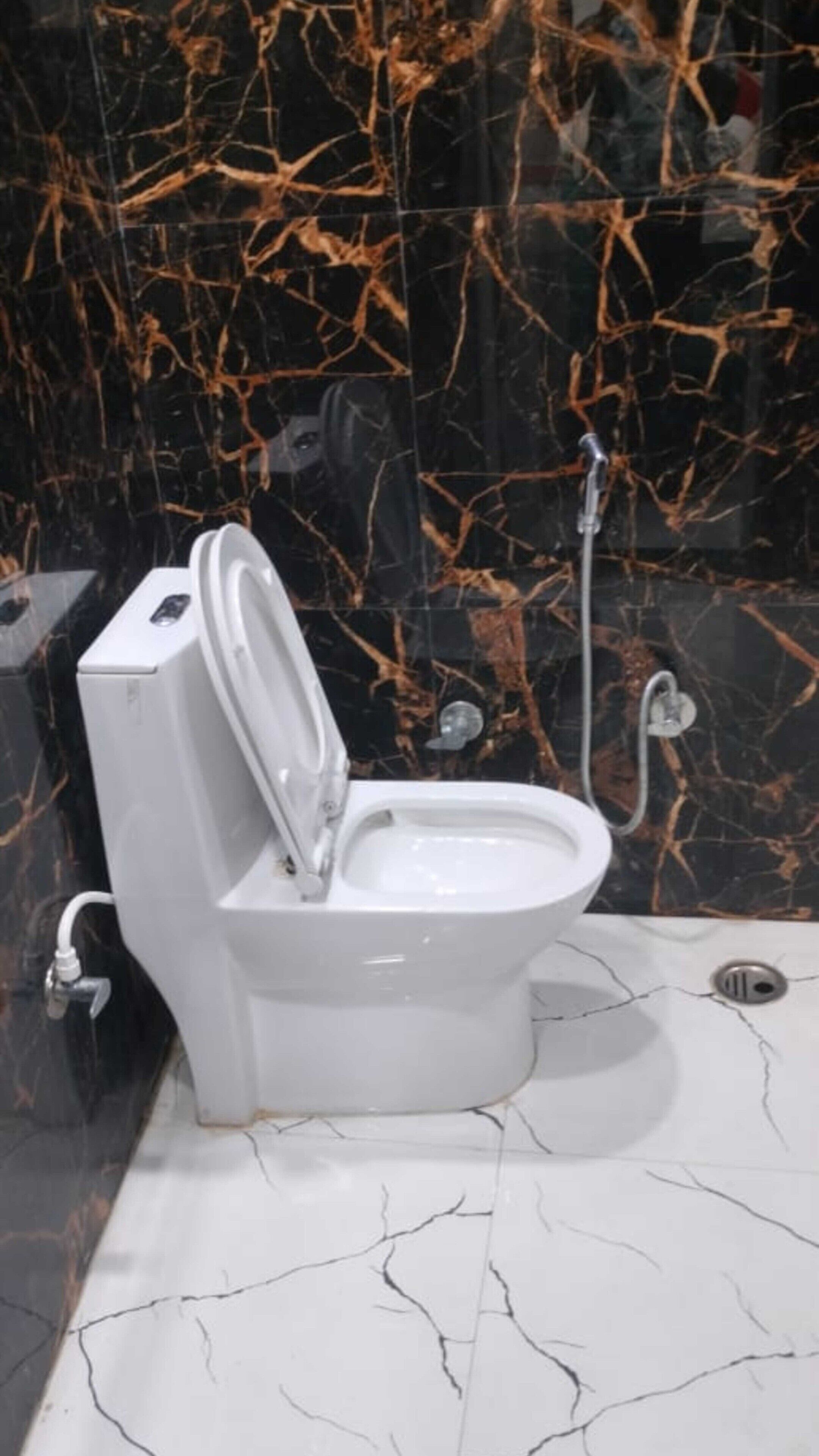 A toilet with a closed lid in a bathroom with black marble walls and white marble flooring.