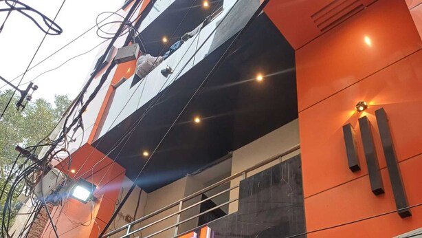 Een hotel met een opvallend bord waarop in grote, vetgedrukte letters "HOTEL NANHU" staat. Het gebouw heeft een modern ontwerp, met een combinatie van oranje en zwarte kleuren. Er zijn meerdere ramen in de gevel en de ingang is zichtbaar, met een glazen deur.