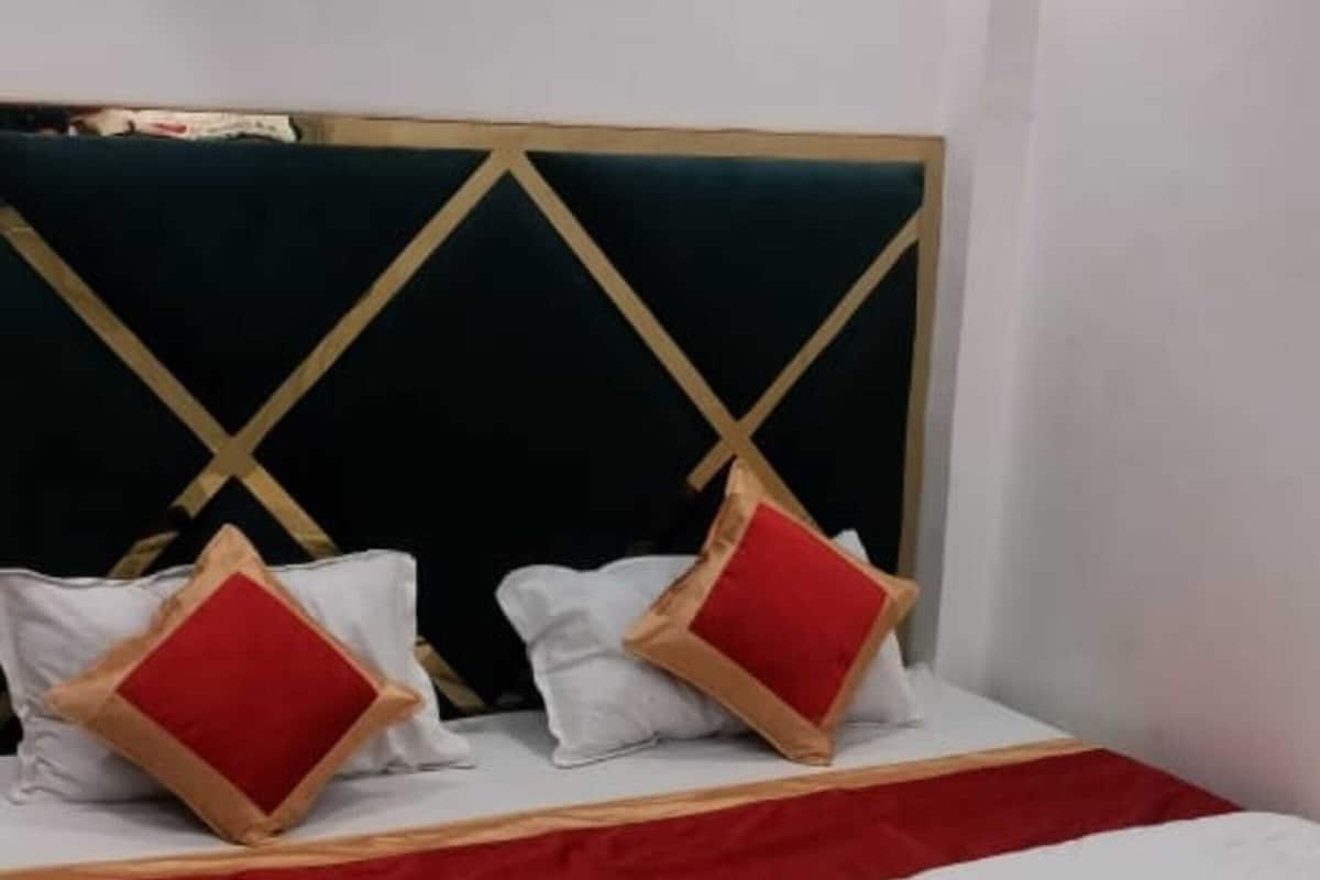 Une chambre d’hôtel avec un lit, une tête de lit ornée d’un motif géométrique et un coussin rouge décoratif.