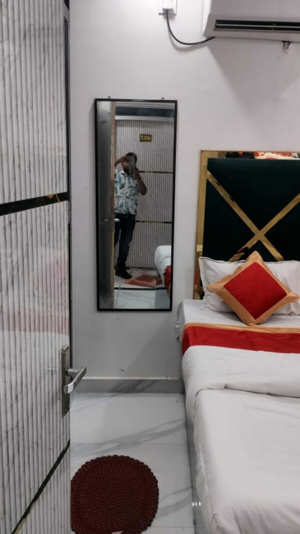 A hotel room with a bed, a mirror, a wardrobe, and a small round rug. - Shri Nanhu Hotel (Prayagraj)