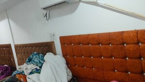 Een kamer met twee bedden, elk met een gestoffeerd hoofdeinde. Er is een witte airconditioningunit aan de muur, en een houten paal die tegen de muur staat.