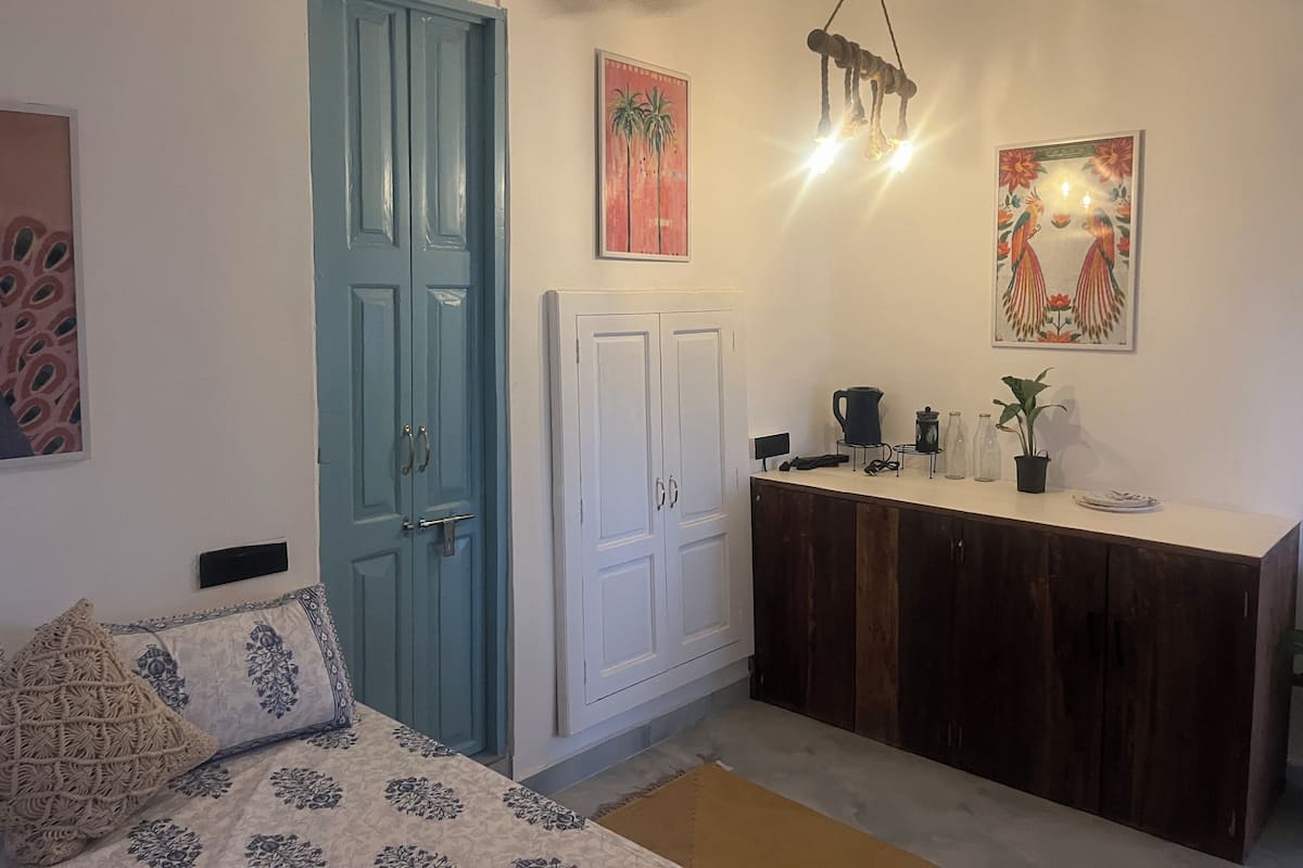 Una stanza con una porta blu, mobili bianchi, un letto con copriletto decorato e due opere d'arte appese al muro.